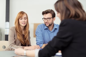 Broker making a presentation to a young couple showing them a document which they are viewing with serious expressions-1