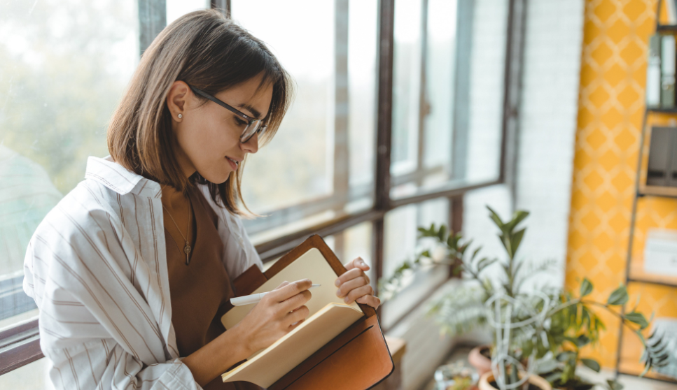 woman wearing glasses writing in a notebook